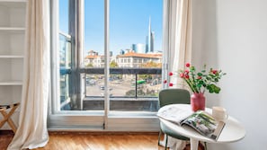 A room with a large window, a table with a magazine, a vase with flowers, and a chair. - Italianway Easy - Porta Nuova 52 D (Milan)