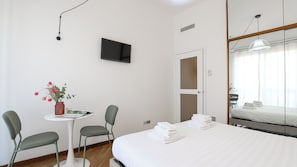 A hotel room with a bed, a TV mounted on the wall, a small table with a chair, and a potted plant. - Italianway Easy - Porta Nuova 52 D (Milan)