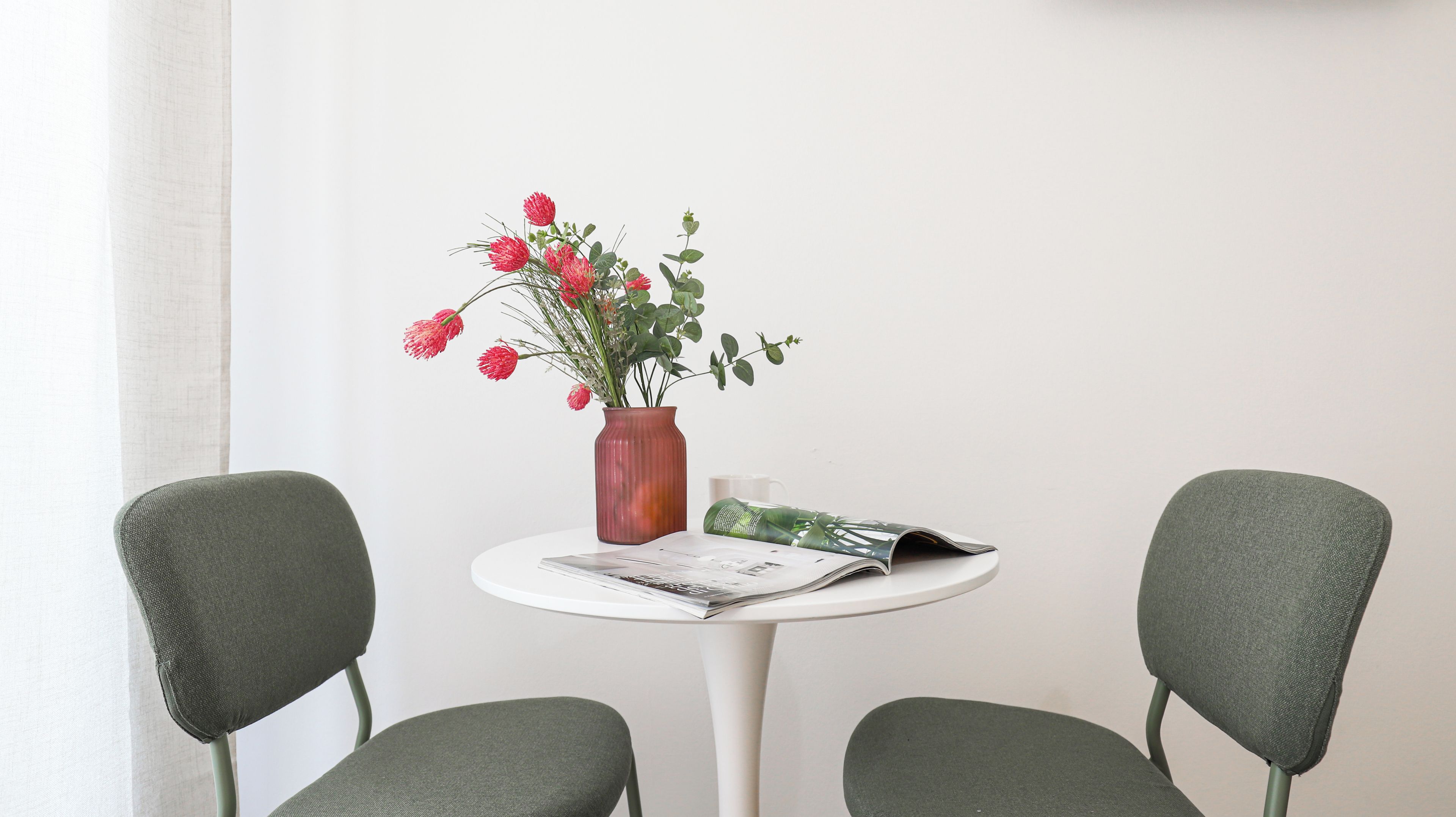 A small round table with a vase of flowers, a magazine, and two chairs.
