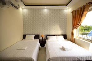 Een hotelkamer met twee bedden, een nachtkastje met lamp en een raam met gordijnen.