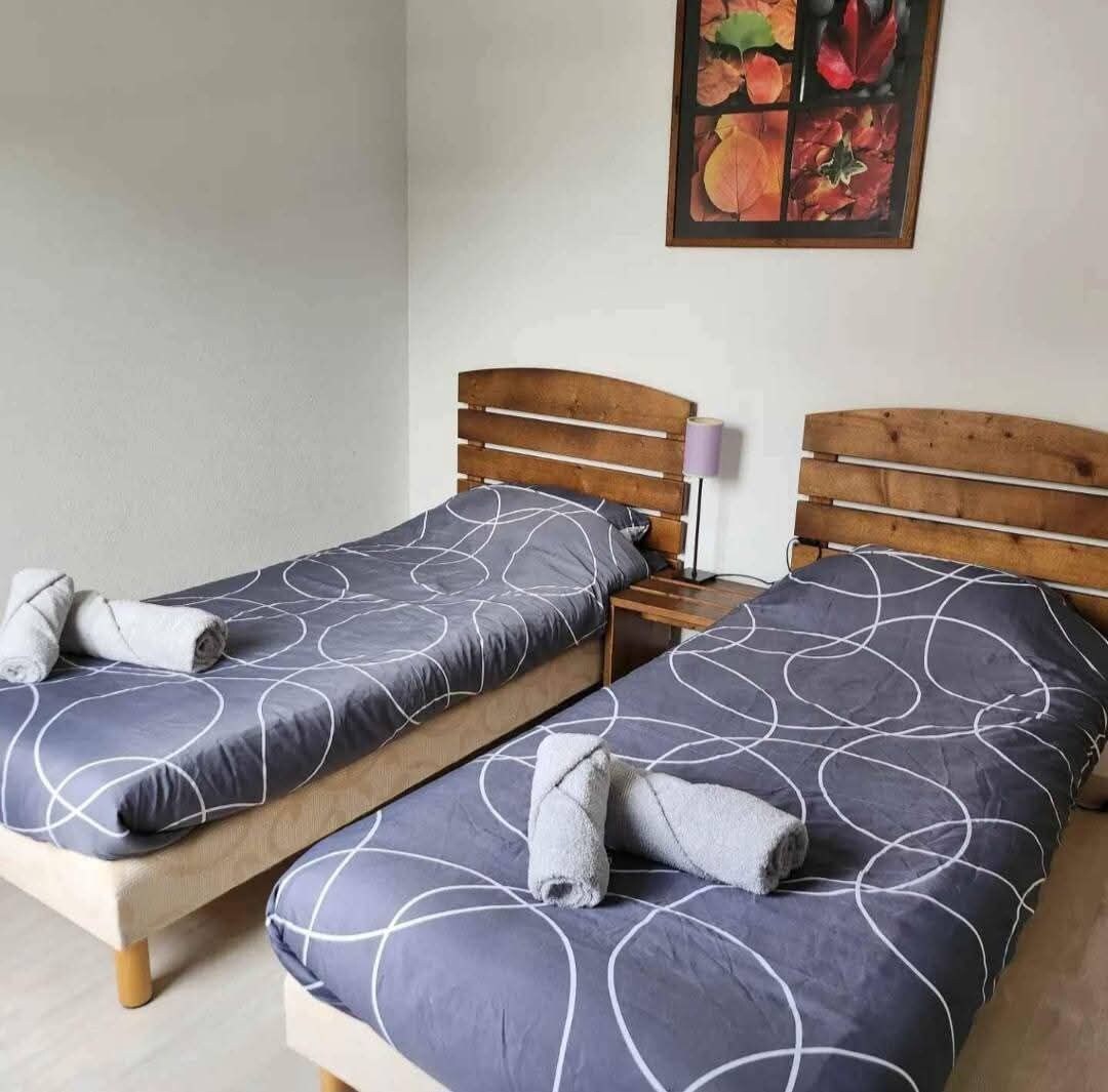 Een kamer met twee bedden, elk met een houten hoofdbord en een deken met een grijs patroon.