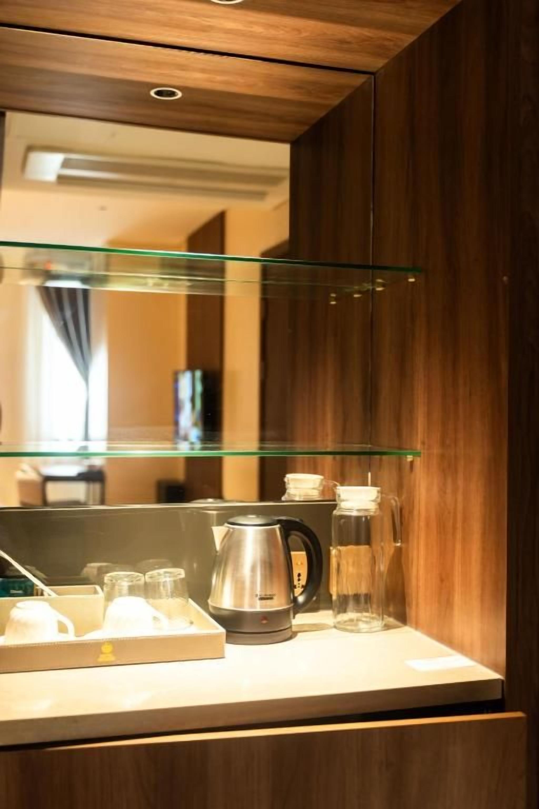 Quarto de hotel com um armário de madeira, uma prateleira de vidro e uma cafeteira no balcão.
