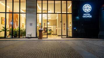A hotel entrance with a reception desk, a glass facade, and a sign indicating the hotel name.