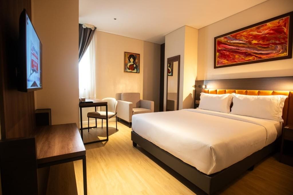 Una habitación de hotel con una cama grande, un escritorio, una silla, un televisor y obras de arte en las paredes.