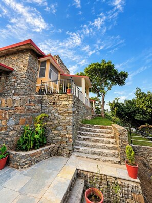 A stone building with a red roof, a balcony, and a staircase leading to a higher level. - Stone Age Villa (Kumbhalgarh)