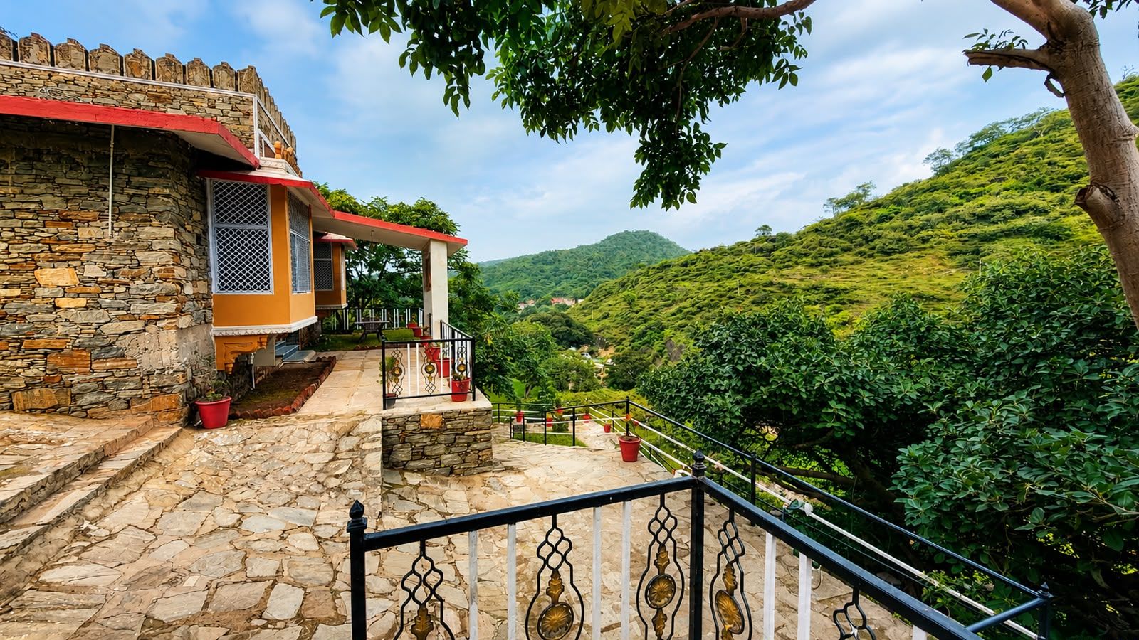 Un edificio de piedra con techo rojo, un balcón con barandilla y vistas a una ladera verde.