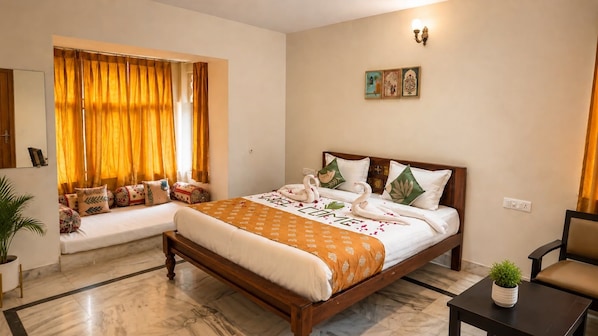 Habitación de hotel con cama, zona de estar con cojines, una mesita con una planta y cuadros en la pared.