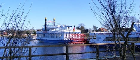 Un muelle con un barco grande amarrado, un banco de madera y árboles sin hojas.