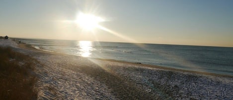 Una playa con el sol bajo en el horizonte, iluminando el agua con un resplandor.