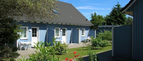 A blue building with a sloped roof, a paved patio area, and a garden with red flowers.