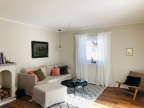 A living room with a sofa, ottoman, coffee table, and a chair. There is a fireplace, a window with curtains, and a picture on the wall. - New Listing (Moos)