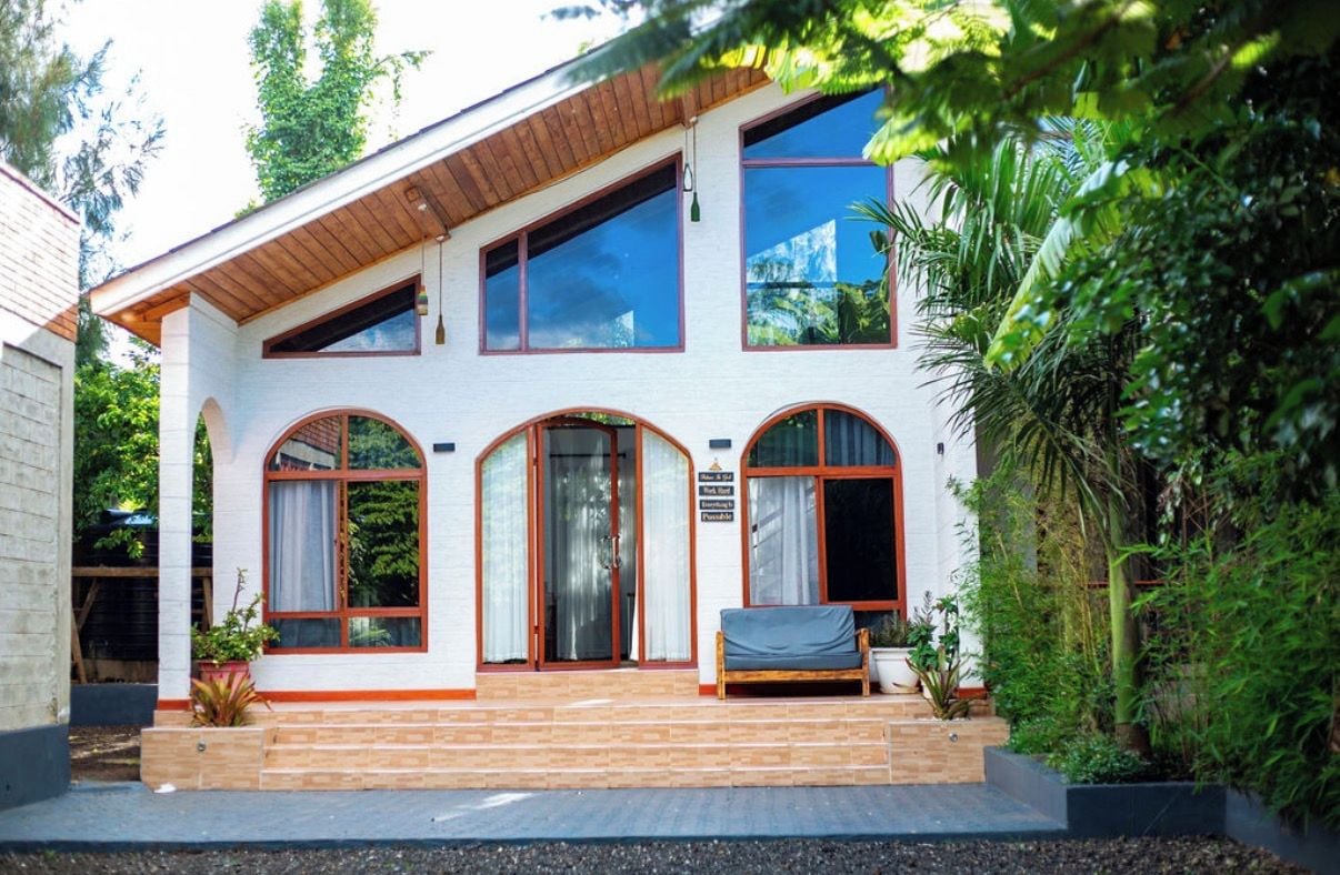 A two-story house with a wooden porch, large windows, and a small garden area.