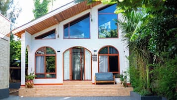 A two-story house with a wooden porch, large windows, and a small garden area.