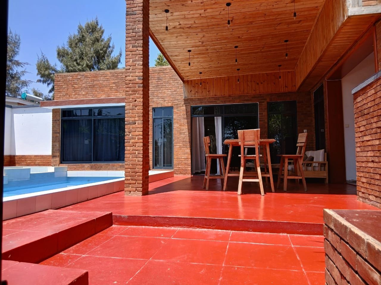 A modern outdoor patio with a pool, wooden furniture, and a brick exterior.