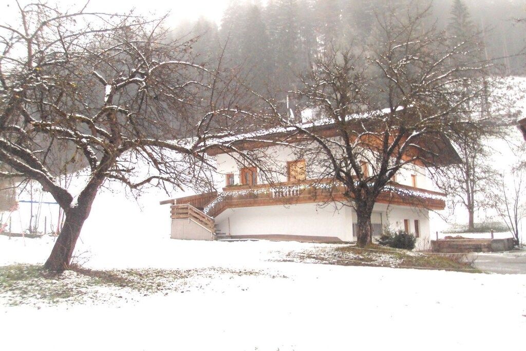 Un bâtiment à la façade blanche et au toit brun, entouré d’arbres sans feuilles, dans un paysage enneigé.