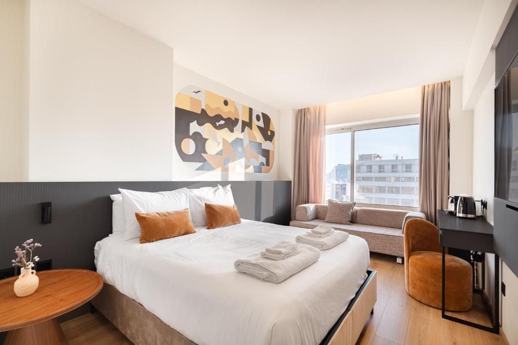 A hotel room with a large bed, a sofa, a chair, a TV, and a window with curtains.