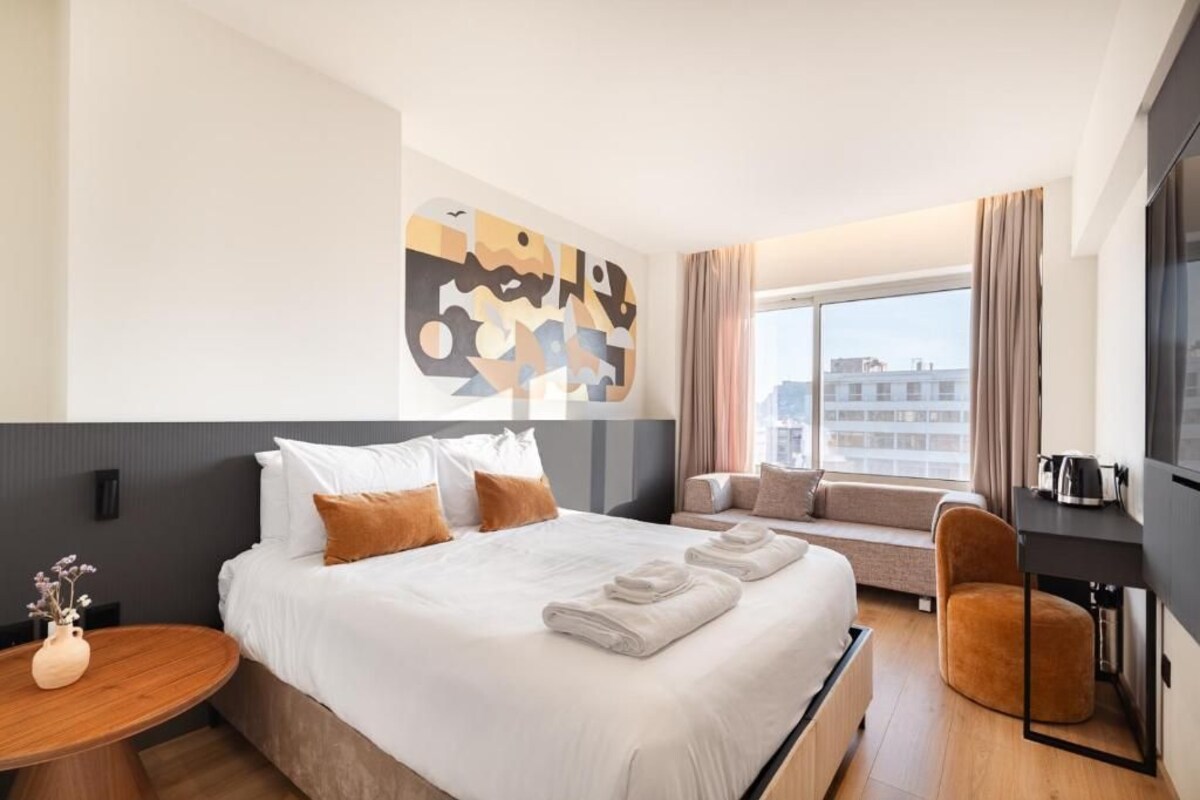 Una camera d'albergo con un letto grande, un divano, una poltrona, una TV e una finestra con tende.