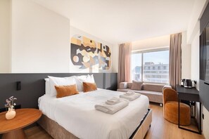 Una camera d'albergo con un letto grande, un divano, una poltrona, una TV e una finestra con tende.