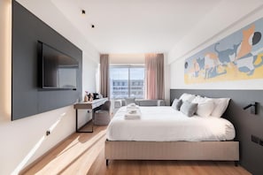 Een moderne hotelkamer met een groot bed, een flatscreen-televisie aan de muur, een bureau met stoel, en een raam met gordijnen.