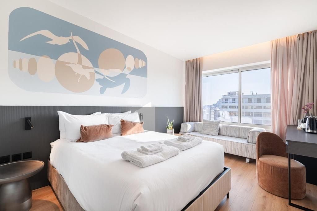 A modern hotel room with a large bed, a window seat, and a city view.