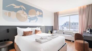 A modern hotel room with a large bed, a window seat, and a city view.