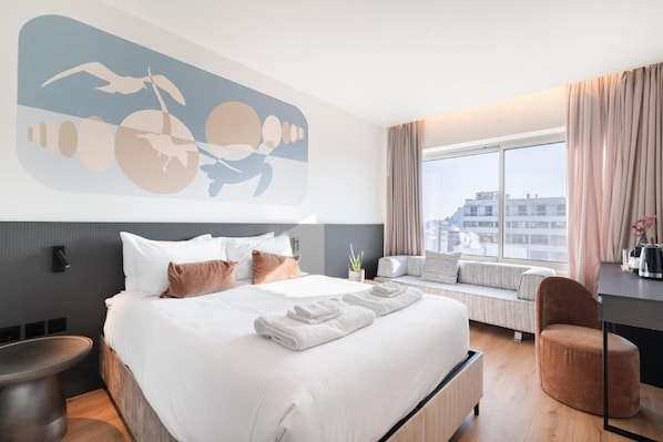 Una camera d'albergo moderna con un letto grande, una seduta vicino alla finestra e vista sulla città.