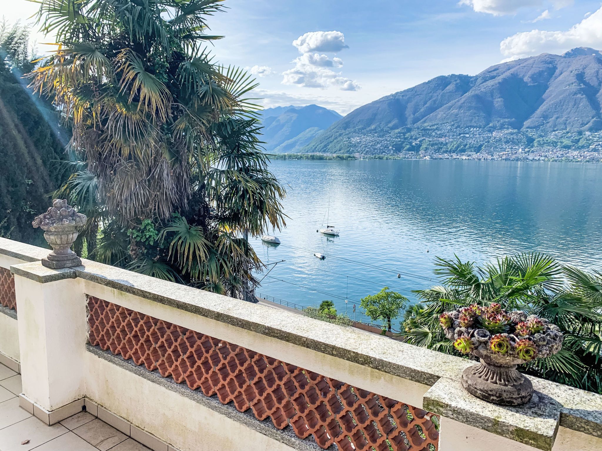 Un balcon avec vue sur un lac, des montagnes et un petit bateau.