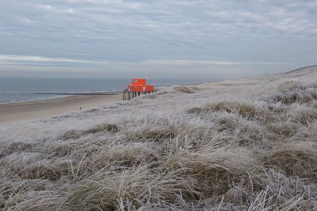 A beach with a red lifeguard tower on a pier.