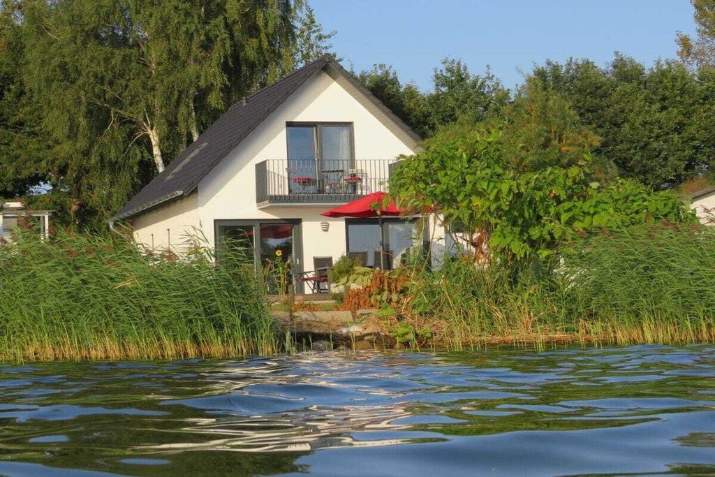 A house with a balcony, a small deck, and a view of a water body.