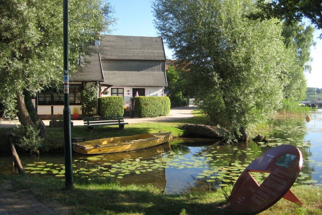 Un edificio a la orilla del río con un muelle, un bote y un estanque lleno de lirios.
