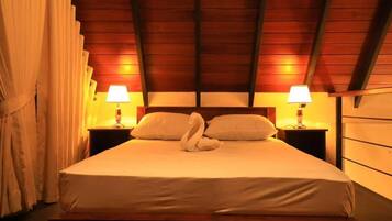 Ein Schlafzimmer mit Holzbalkendecke, zwei Nachttischlampen, einem Bett mit weißer Bettwäsche und einer Schwan-Form-Kissenanordnung.