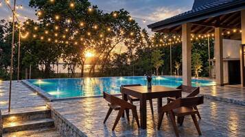 Ein Swimmingpool mit einer Steinterrasse, umgeben von Bäumen und Lichterketten.
