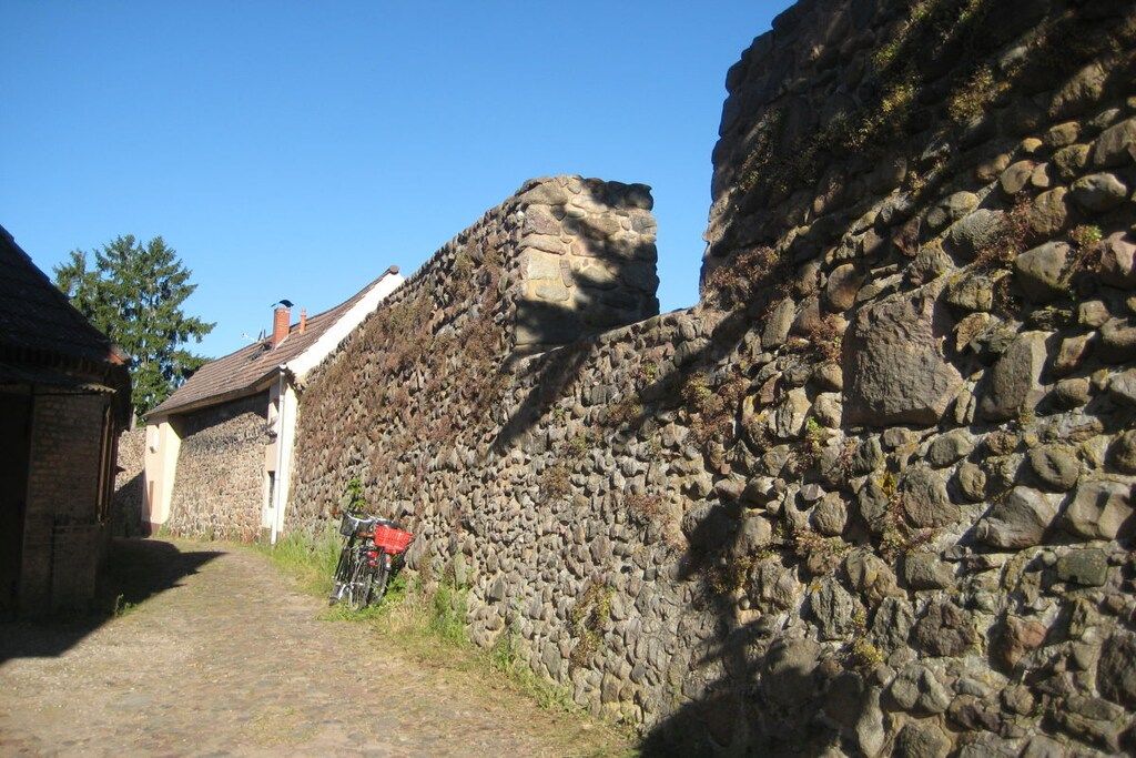 Une ruelle étroite pavée de pierres, bordée de murs en pierre et surmontée d’un bâtiment doté d’un toit en pente.