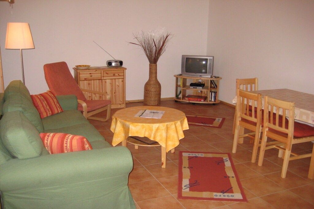 Uma sala de estar com sofá, cadeiras, uma mesinha, televisão e um armário.