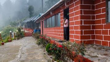 A row of red brick buildings with a person standing at the entrance, a stone-paved pathway, and a mountainous backdrop.