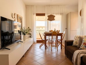 Un salon comprenant un téléviseur, une table à manger, des chaises, un canapé et une fenêtre avec des rideaux.