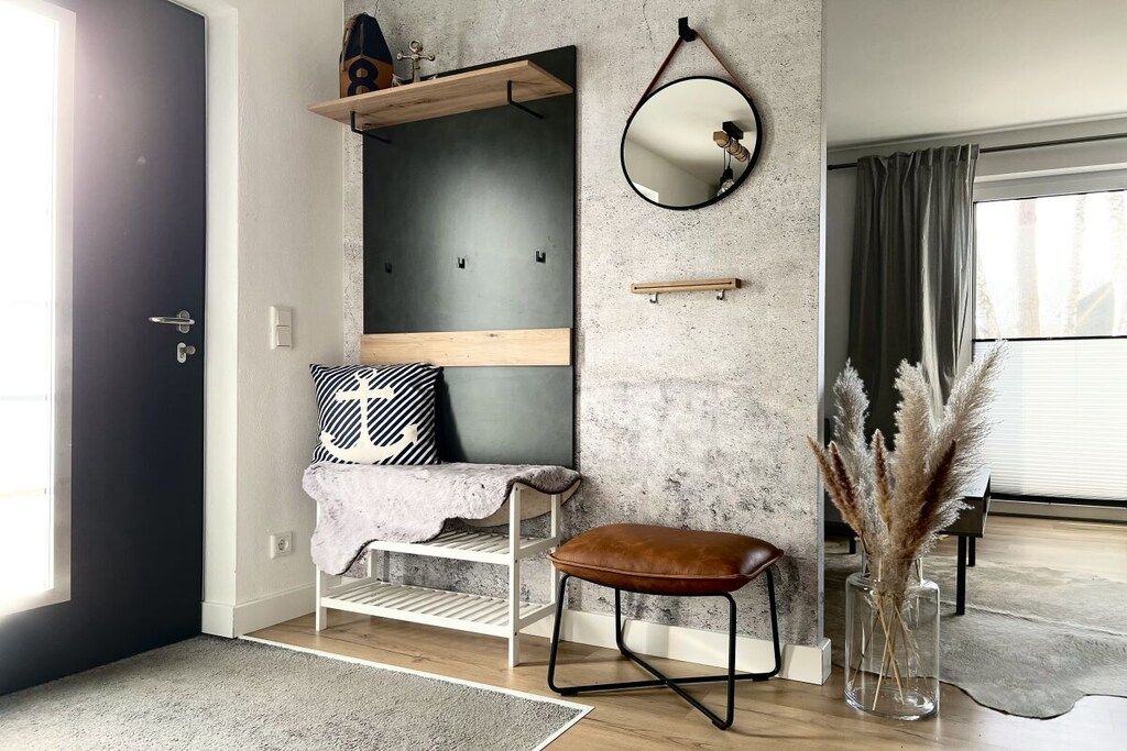 Une pièce moderne avec un mur d’accent en béton, un banc en bois, un miroir et un vase contenant des plumes d’herbe de la pampa.
