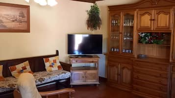 Een woonkamer met een bank, een stoel, een televisie, houten kasten en een plafond met zichtbare balken.