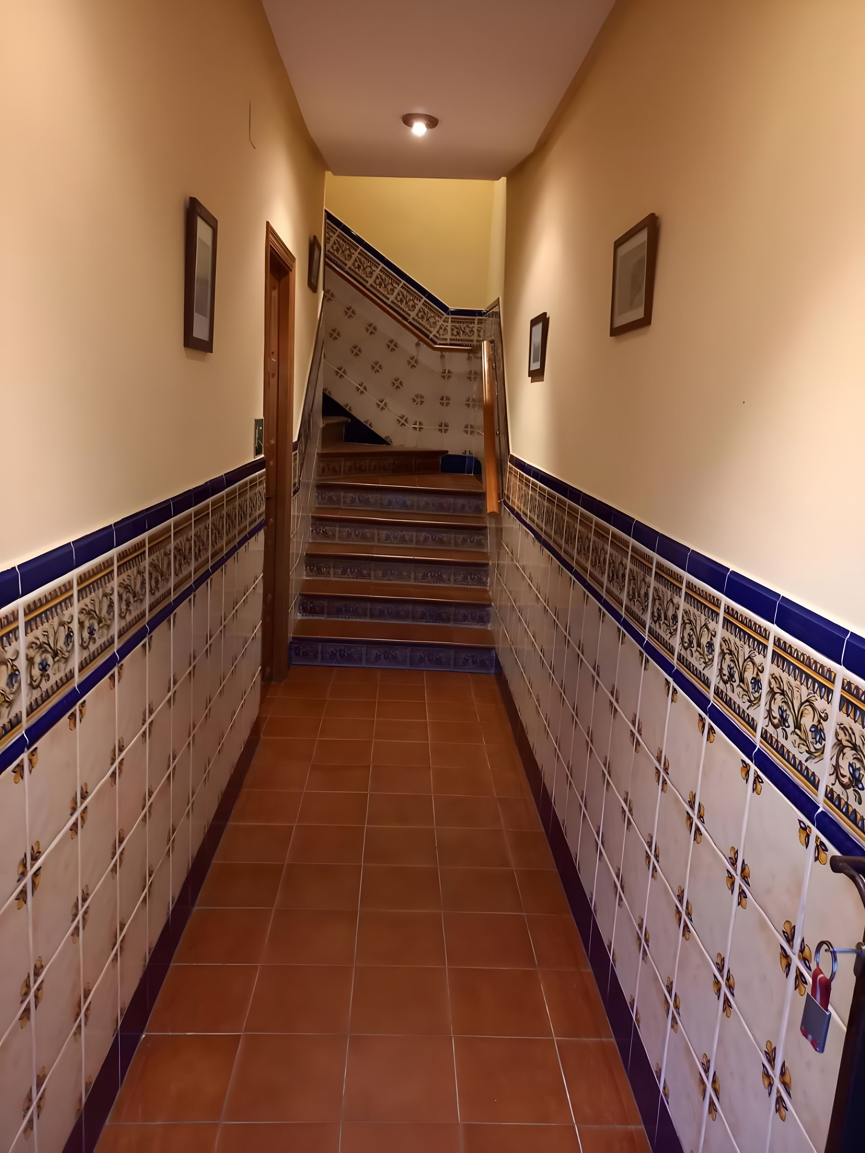 Un couloir au sol et aux murs carrelés, qui mène à un escalier dont les marches sont décorées de motifs.
