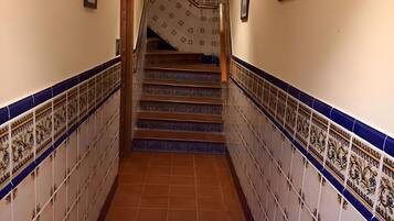 Un couloir au sol et aux murs carrelés, qui mène à un escalier dont les marches sont décorées de motifs.