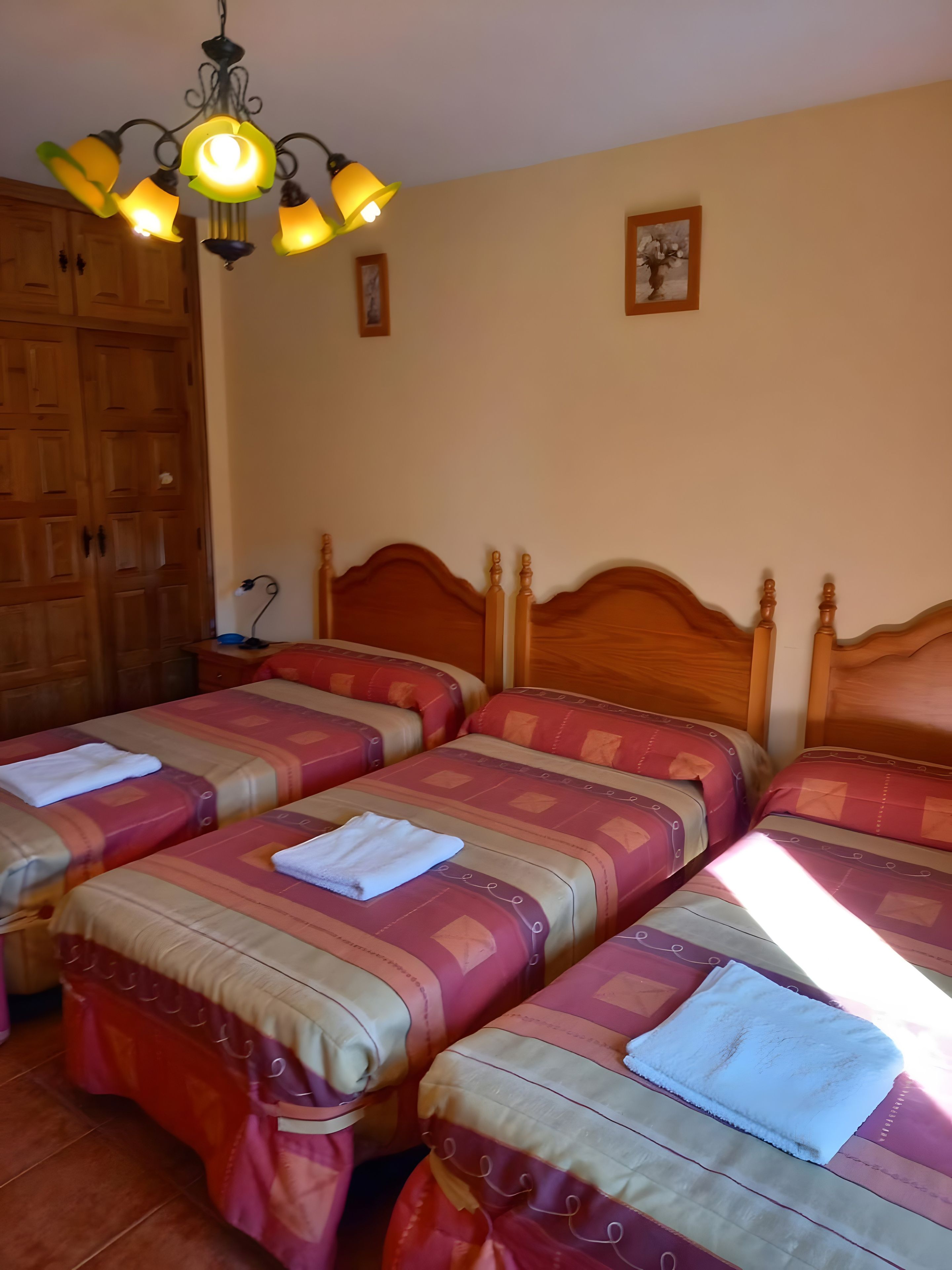 A hotel room with four beds, wooden headboards, and a chandelier.