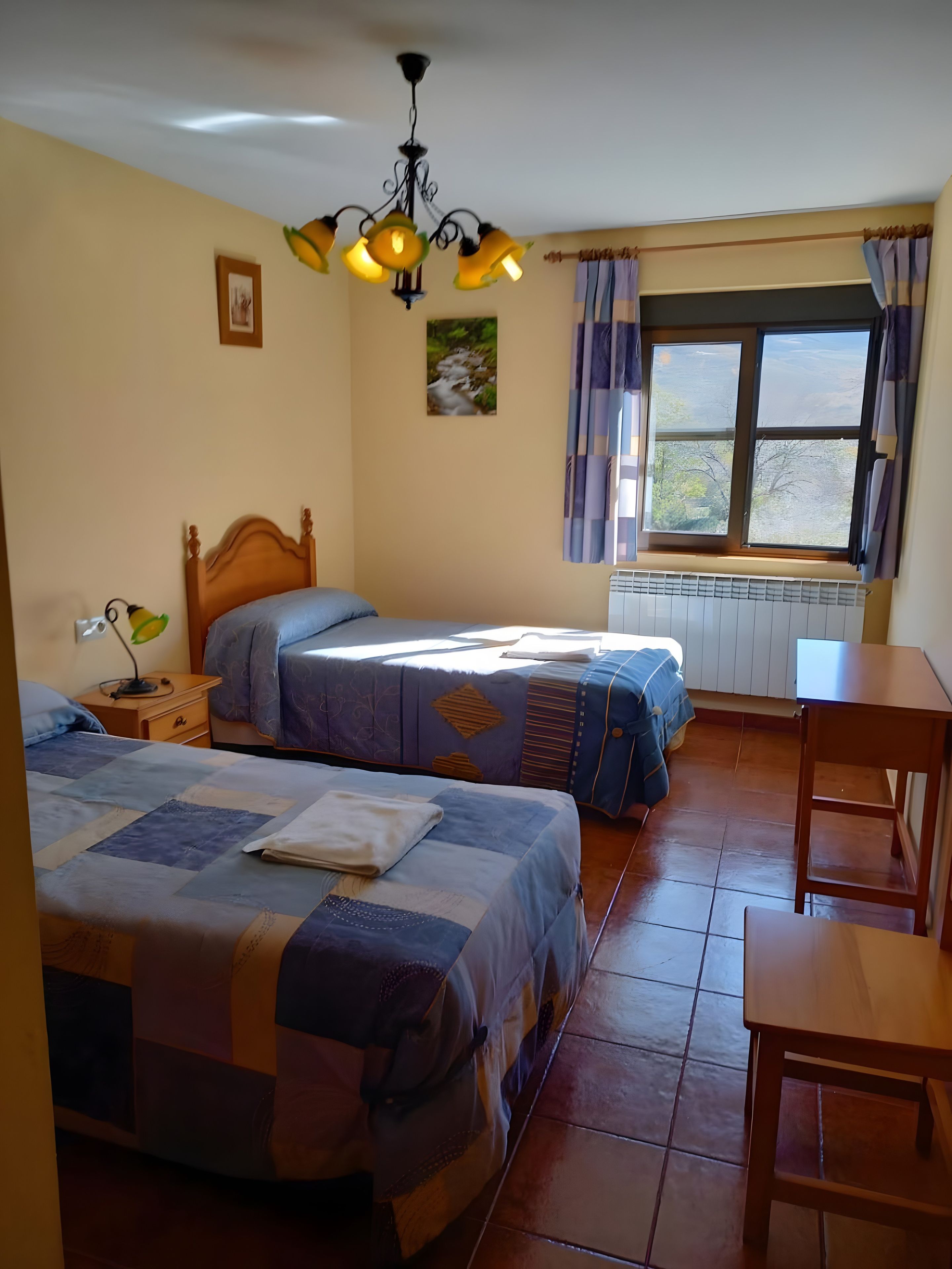 Een kamer met twee bedden, een tafel, een raam met gordijnen en een radiator.