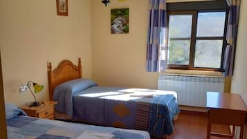 Een kamer met twee bedden, een tafel, een raam met gordijnen en een radiator.