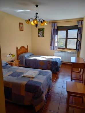 Une chambre avec deux lits, une table, une fenêtre avec des rideaux et un radiateur.