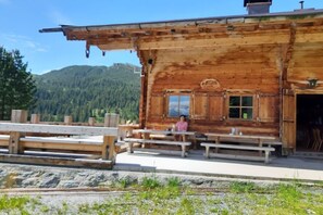 A rustic wooden cabin with a bench seating area and a view of a mountainous landscape.
