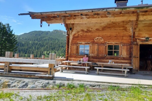 A rustic wooden cabin with a bench seating area and a view of a mountainous landscape.