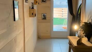 Un couloir aux murs en bois, un sol carrelé, une table avec une lampe et une porte donnant sur l’extérieur.