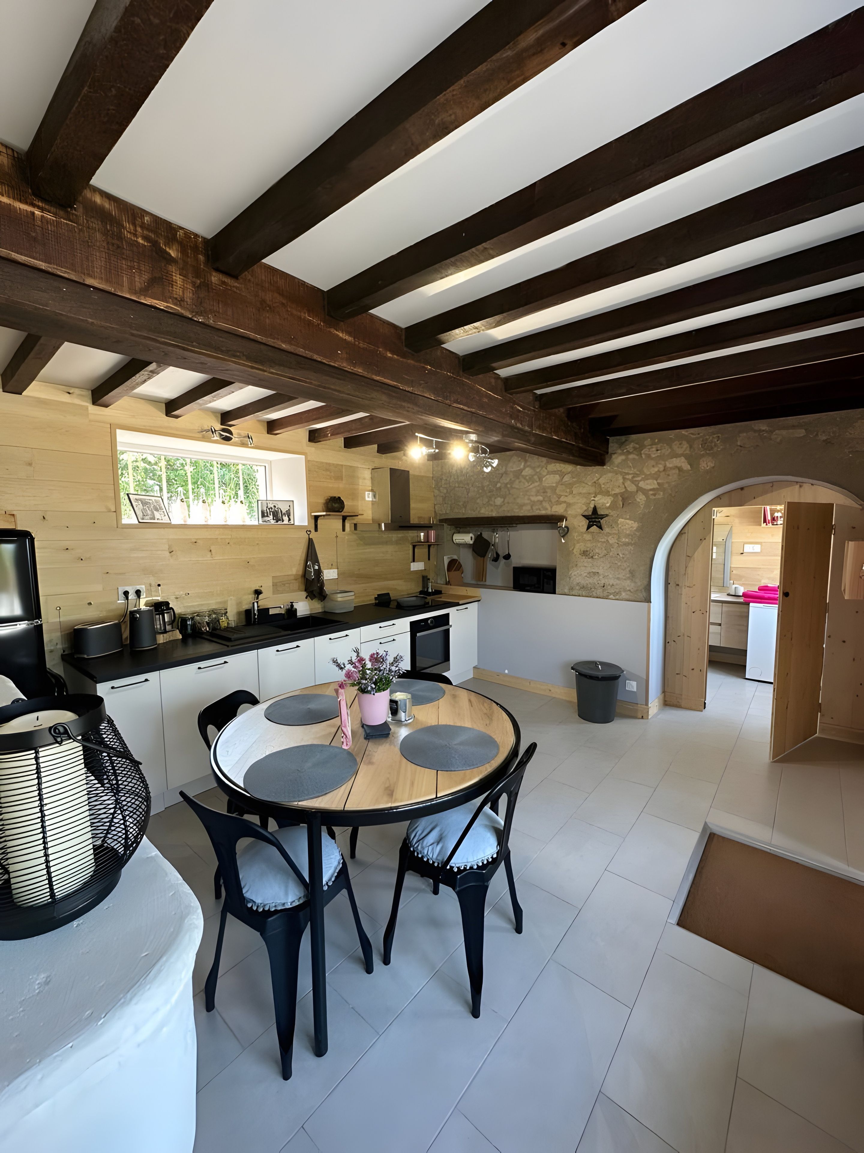 Une cuisine moderne avec un îlot central, des poutres en bois et un mur en pierre.