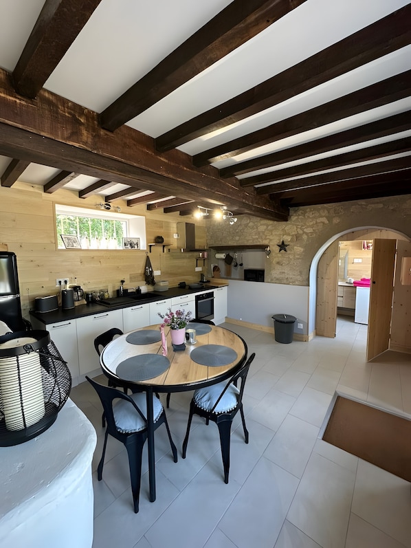 A modern kitchen with a central island, wooden beams, and a stone wall.