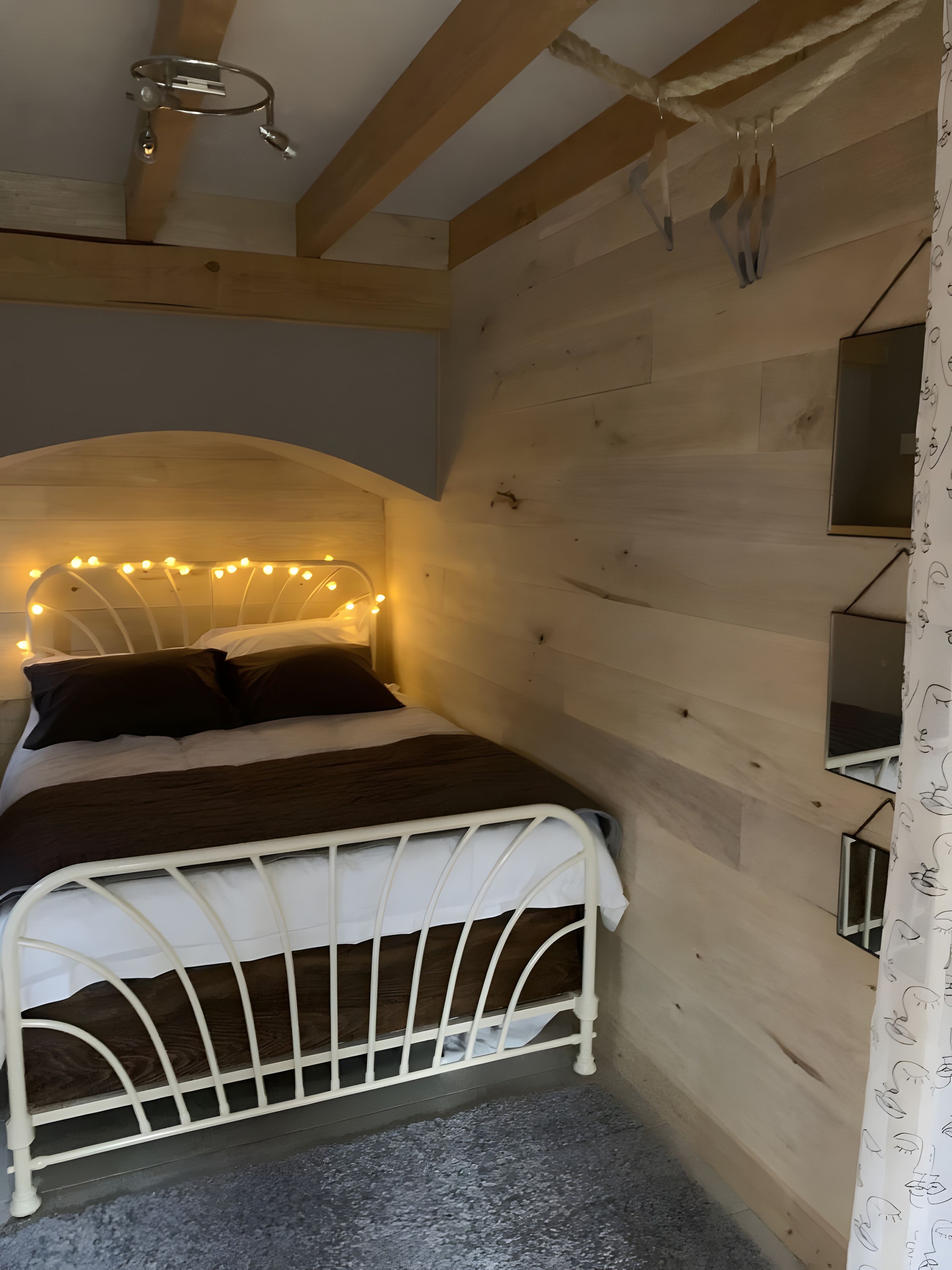 Une chambre avec un lit en métal blanc, une tête de lit en bois et des guirlandes lumineuses.
